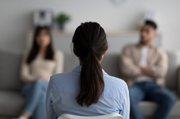 Female psychologist sitting with her back to camera, consulting young arab couple at office, selective focus